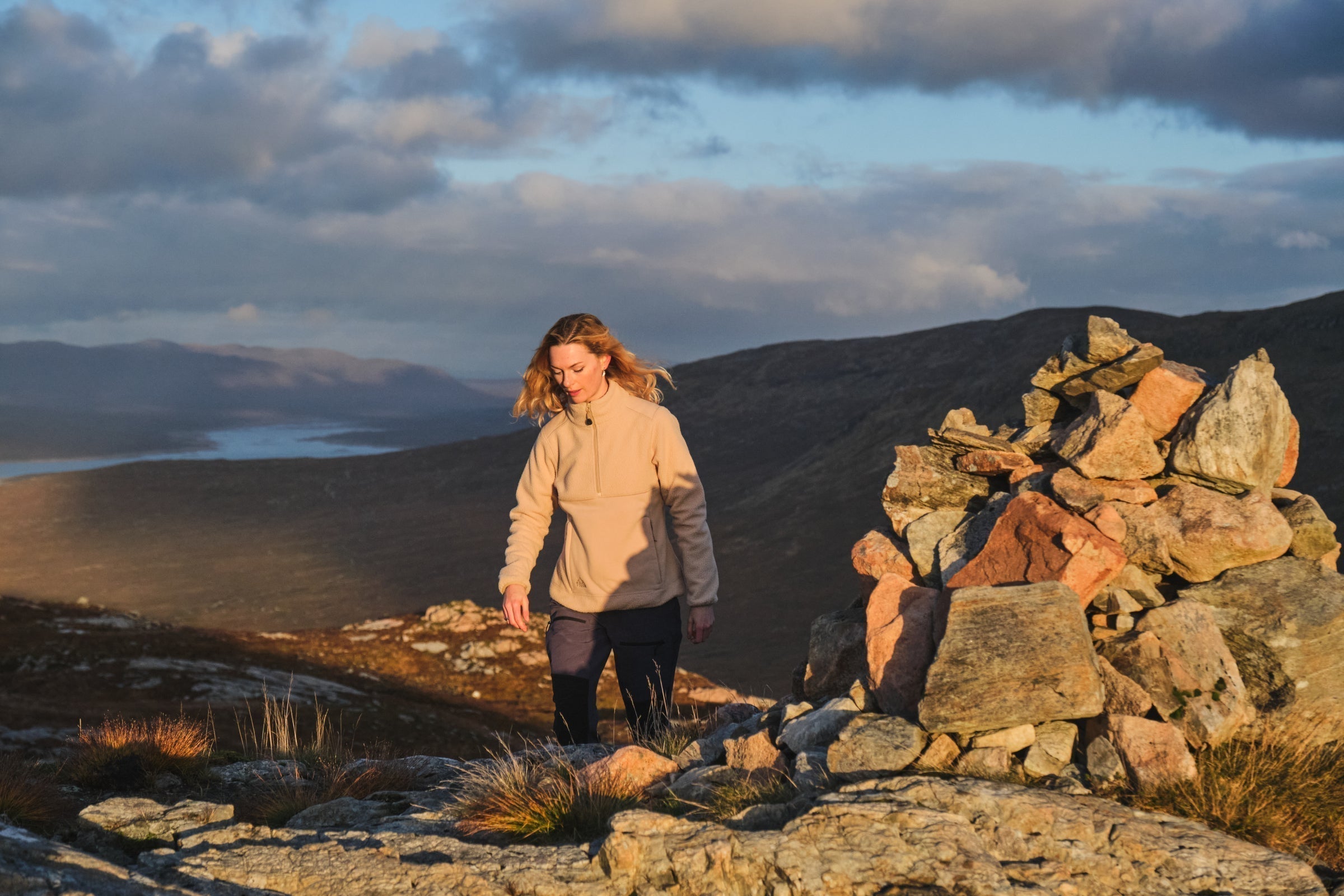 Person hiking near a rock cairn in golden light