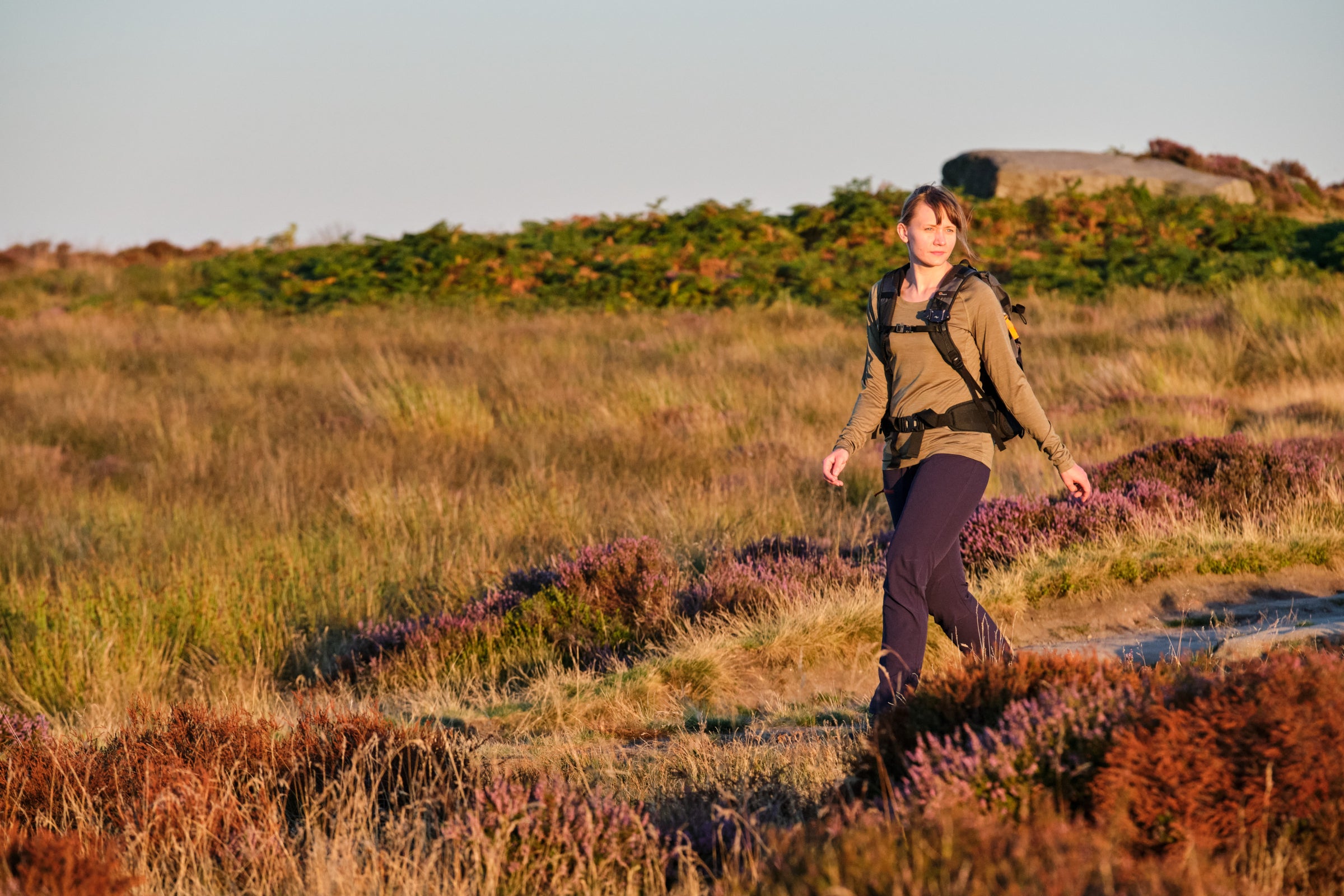 A person hiking through a grassy field wearing Fjern clothing