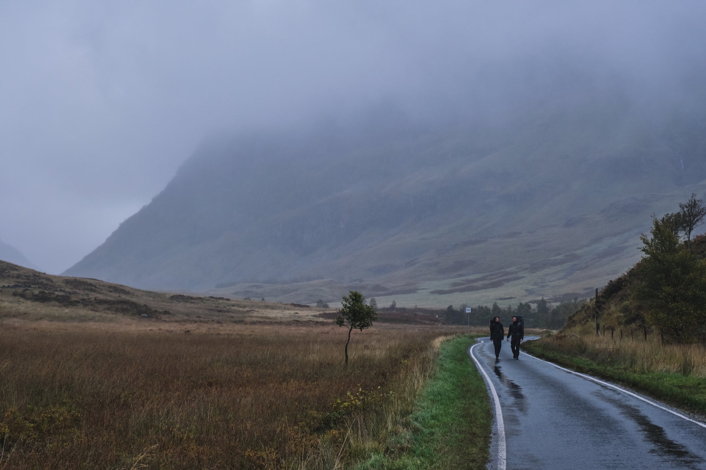 Two people walking on a wet road through a foggy valley, wearing Fjern Orkan waterproof jackets