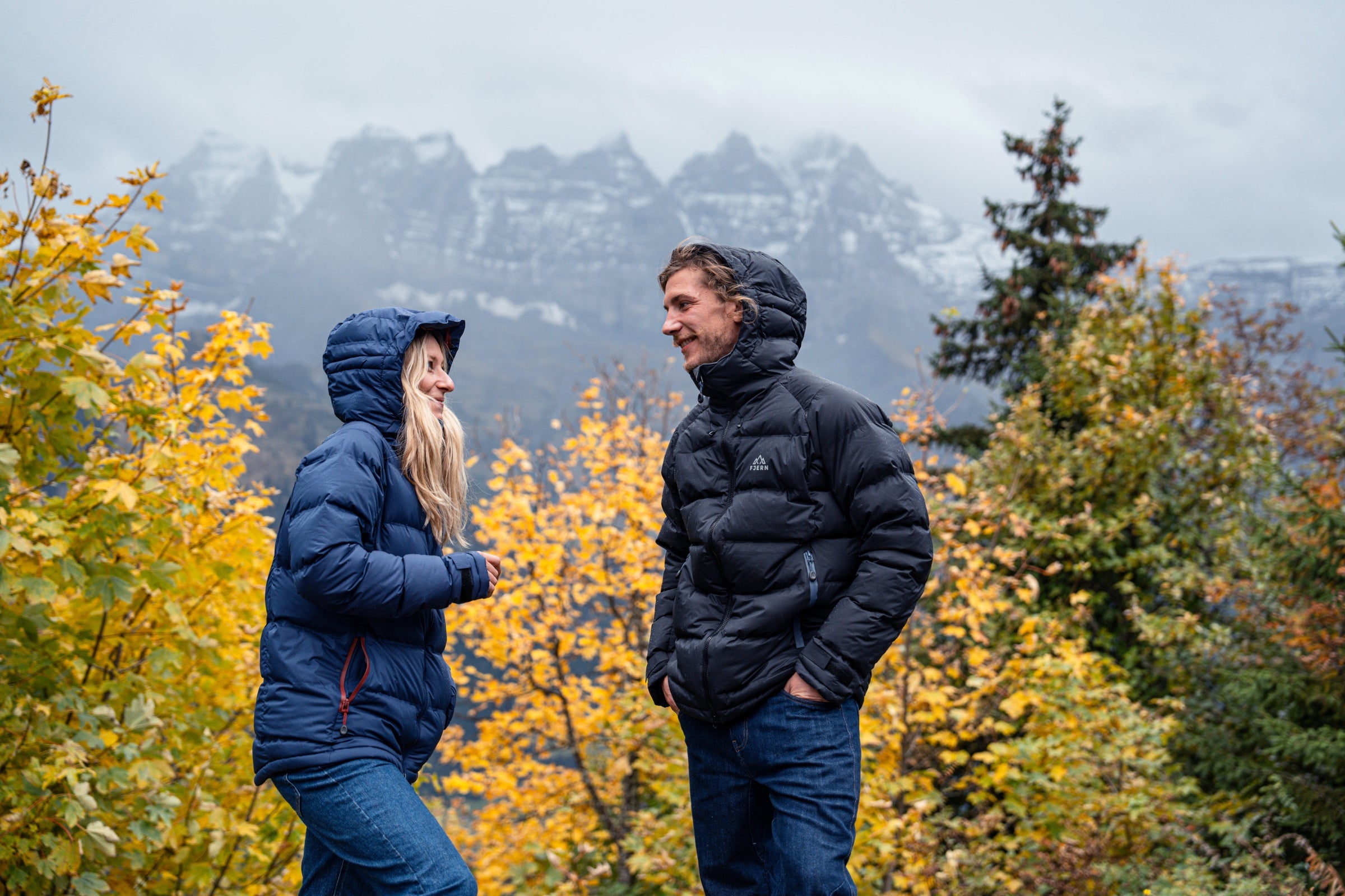 A man and woman wearing waterproof down jackets in an autumn mountain landscape