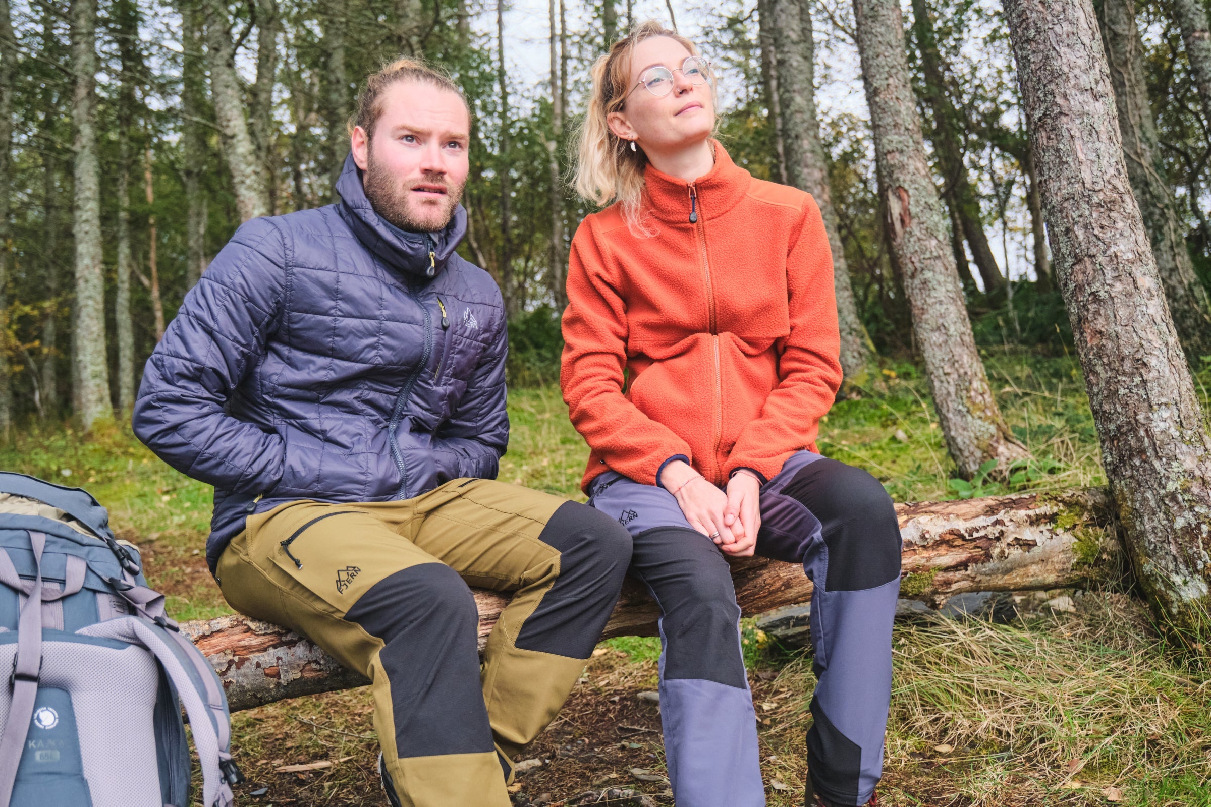 Two people in Fjern clothing seated on a log in a woodland area