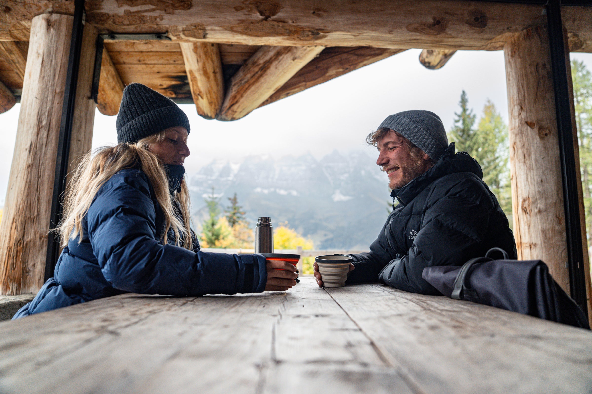 Two people sitting at a wooden table with hot drinks