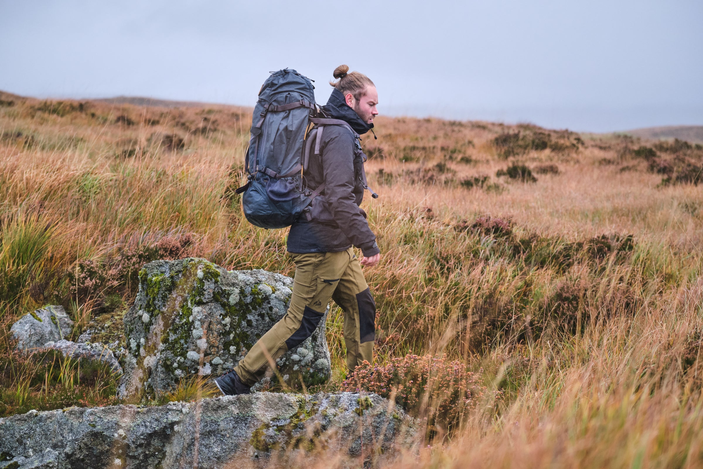 A person hiking with a large backpack in a grassy, rocky landscape