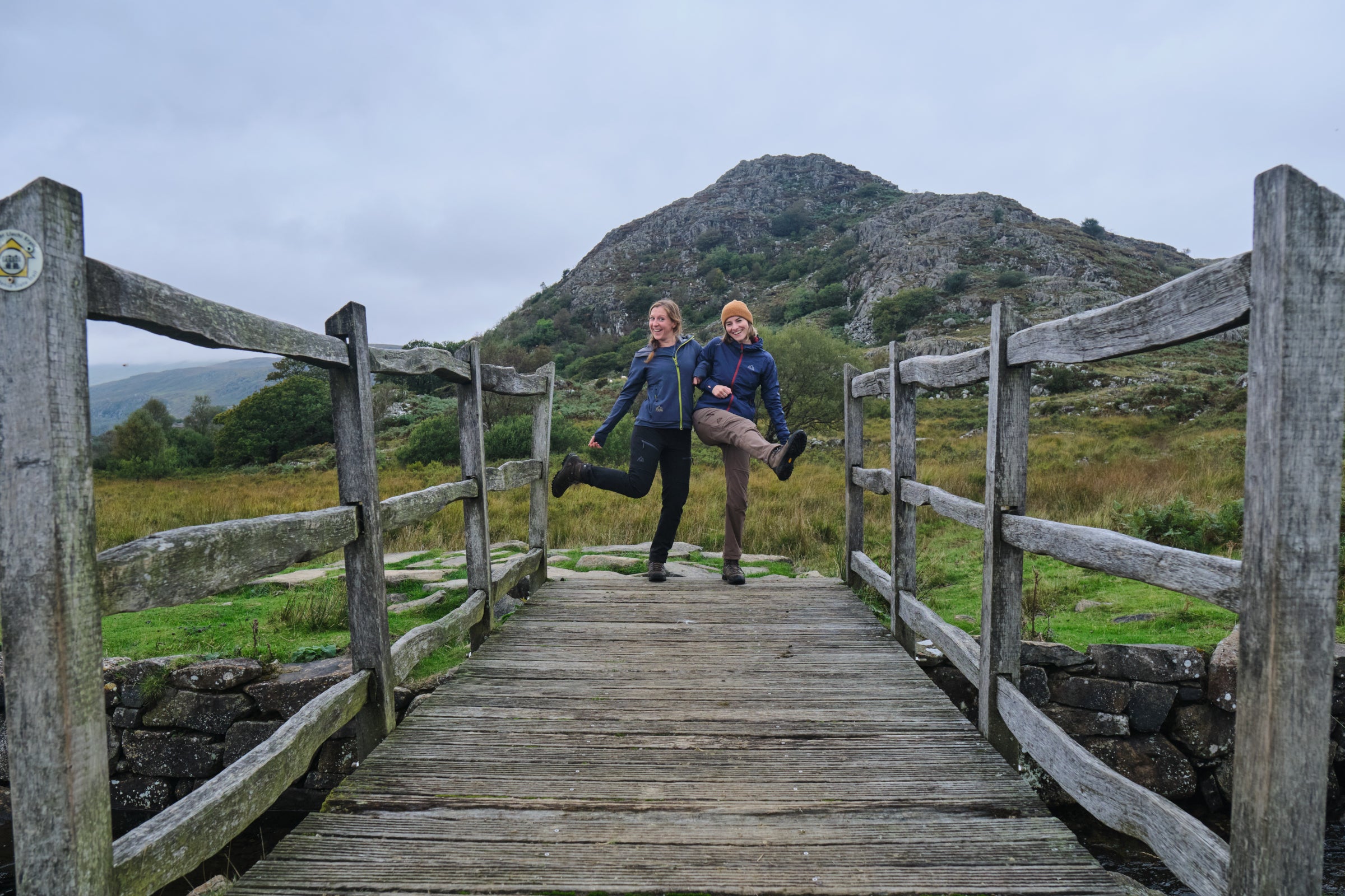 Two people posing playfully on a wooden bridge in Fjern hiking kit