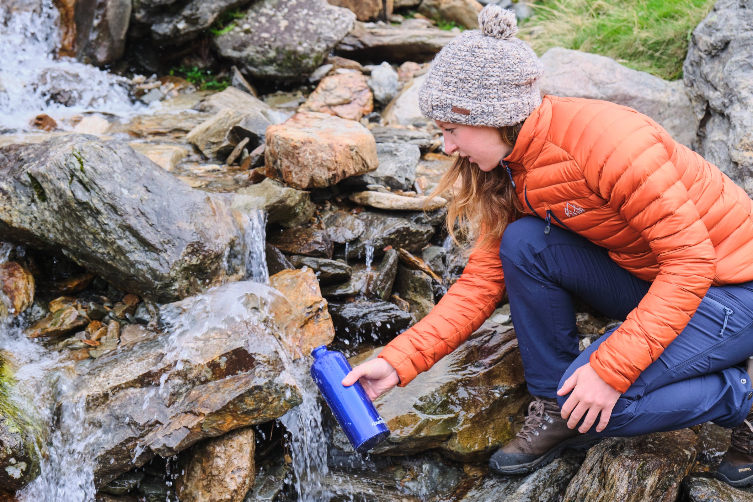 A person filling a water bottle from a mountain stream