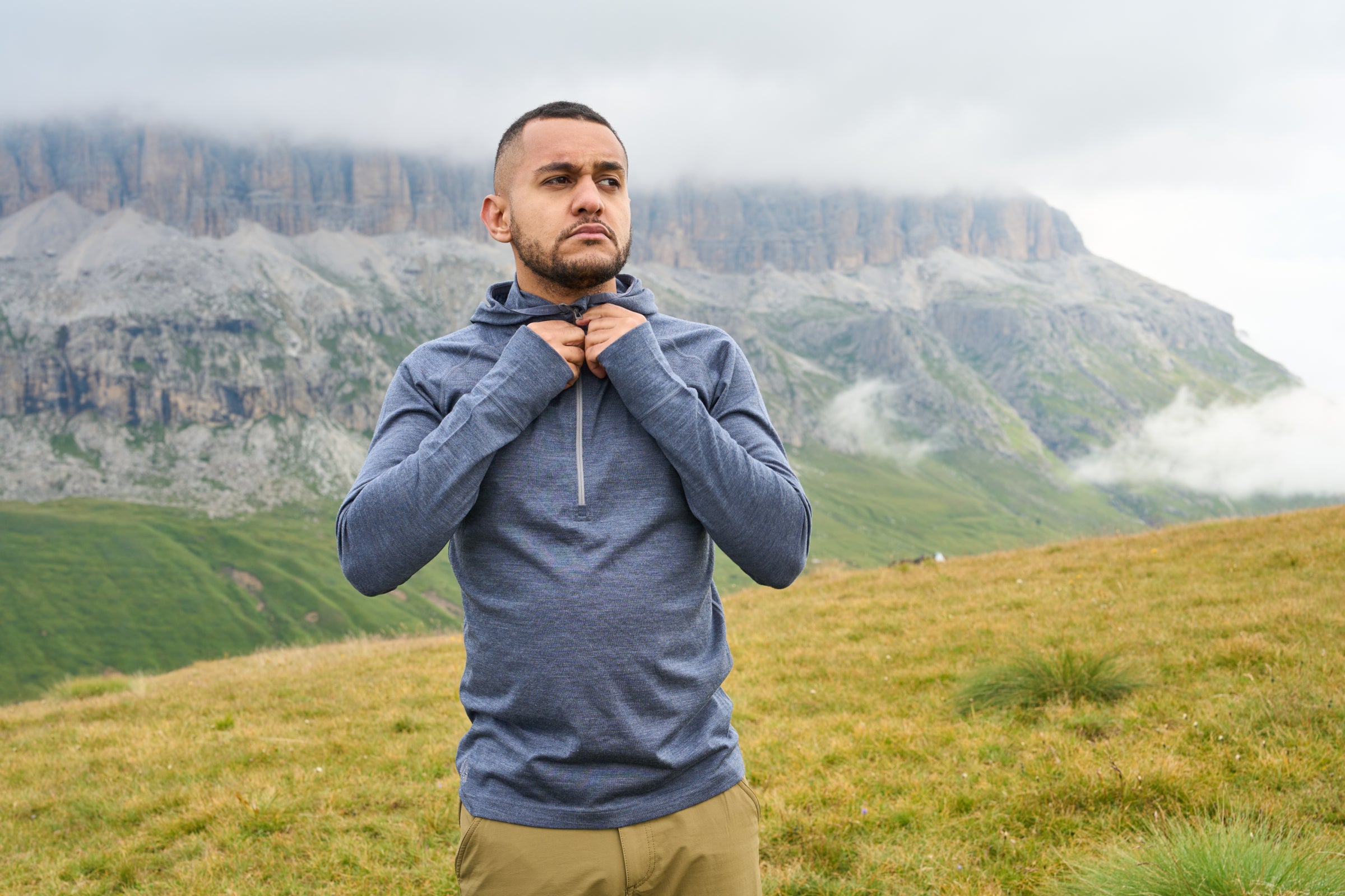 Man in a blue merino pullover zipping it up in a mountainous landscape