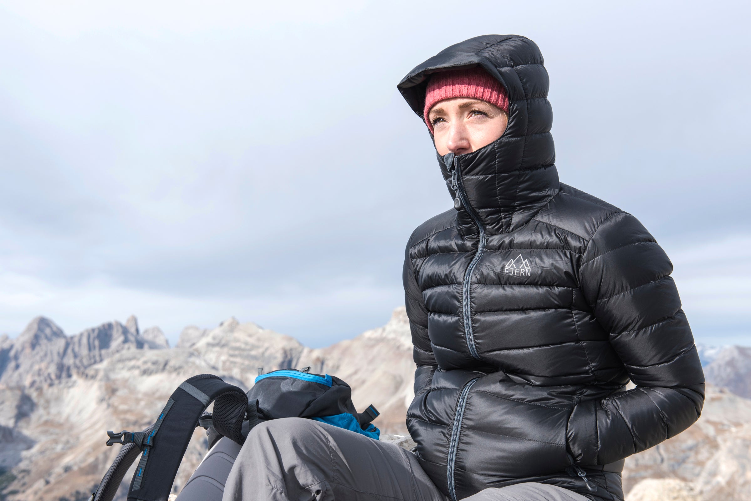 Woman bundled up in a black down jacket with a hood and beanie, sitting outdoors