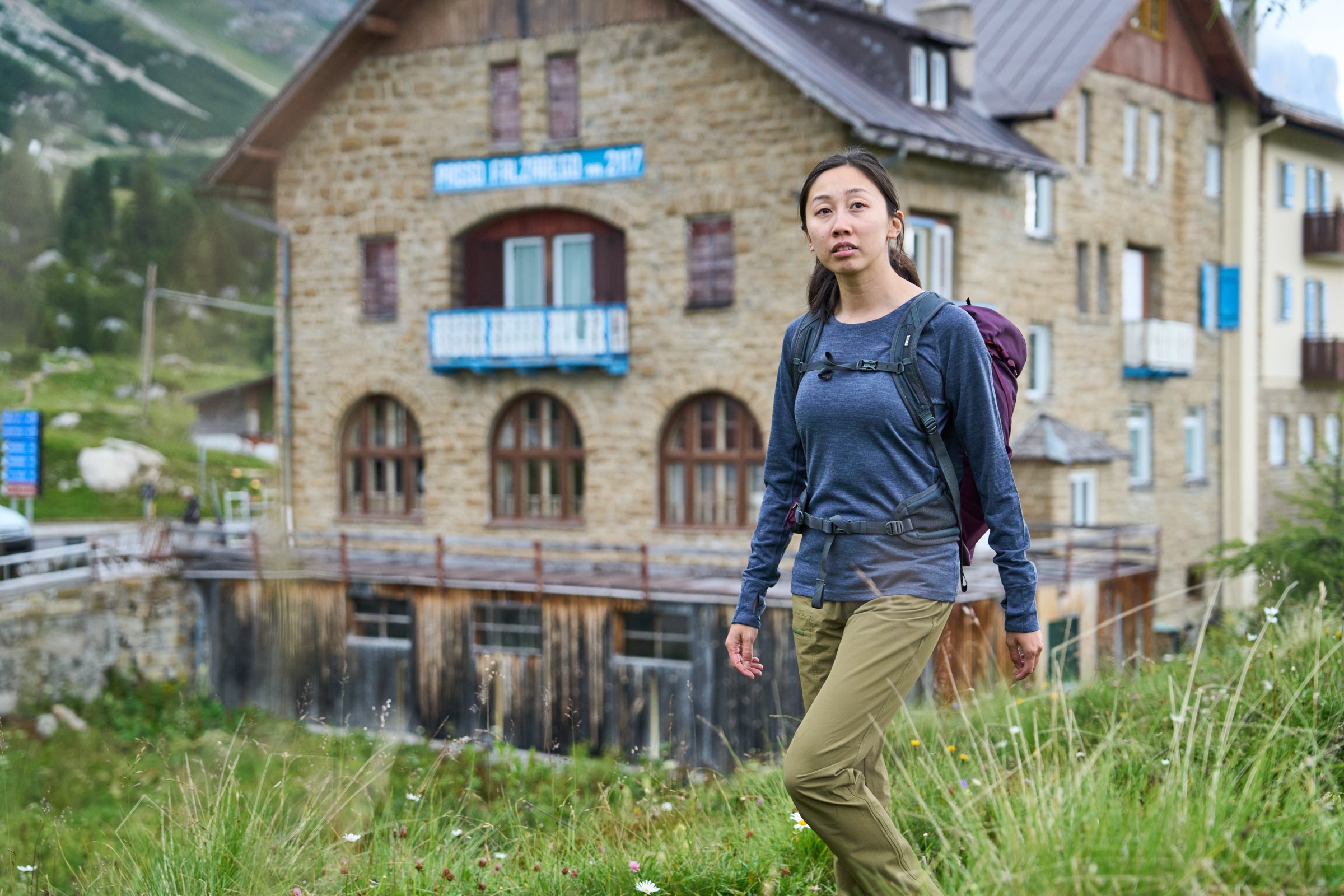 Woman in a blue merino crew top hiking past a rustic stone building