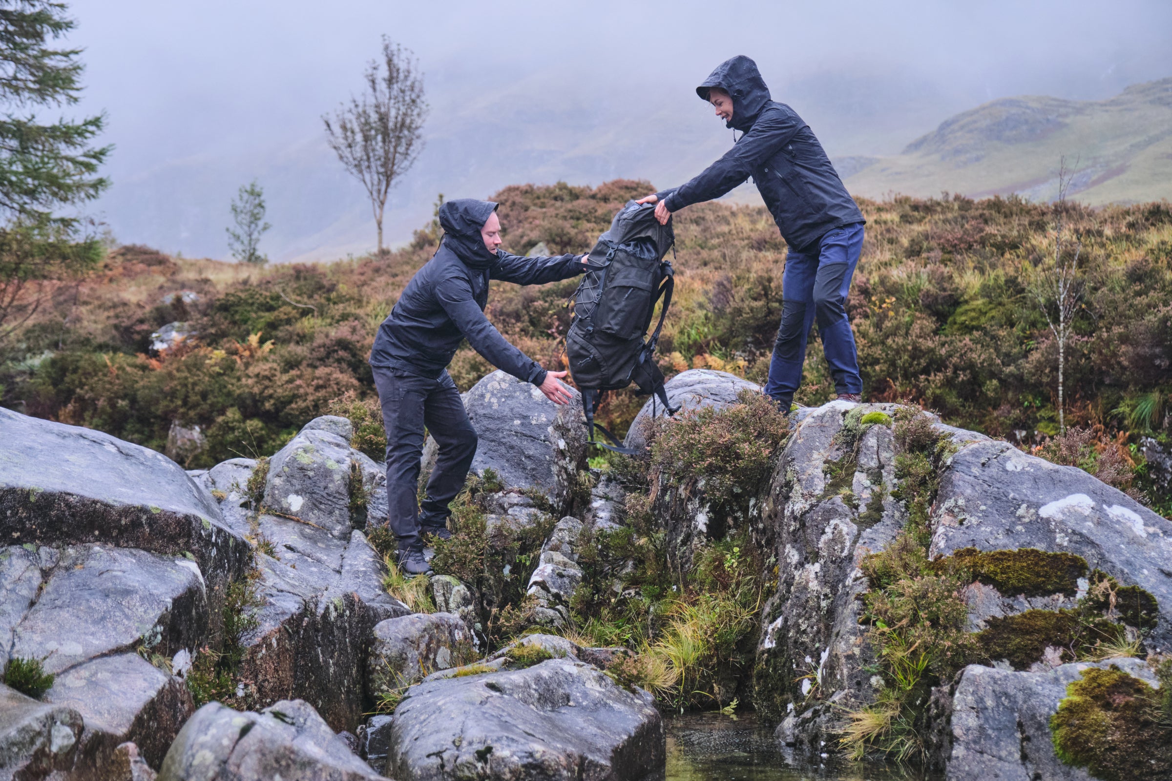 Two hikers crossing rocks in wet weather