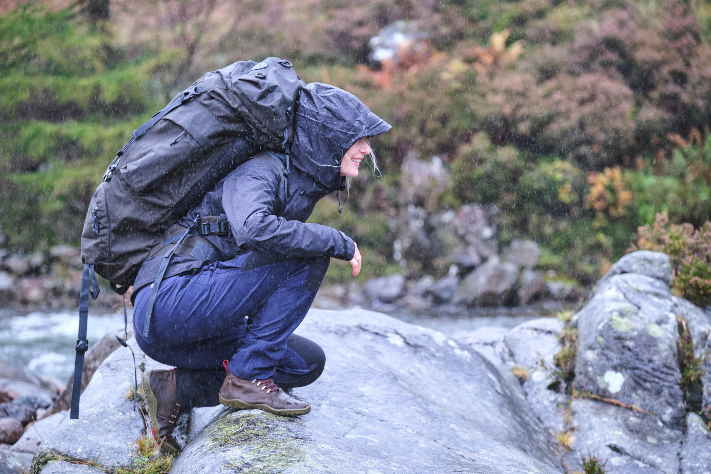 A hiker in a Fjern Orkan Waterproof Jacket examines a stream on a rainy day