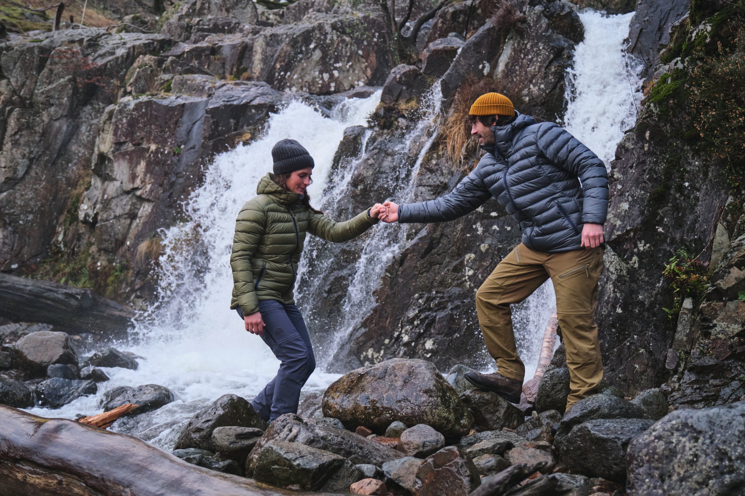 Hikers in Fjern Arktis II Jackets and Vinter Trousers assist each other across a stream